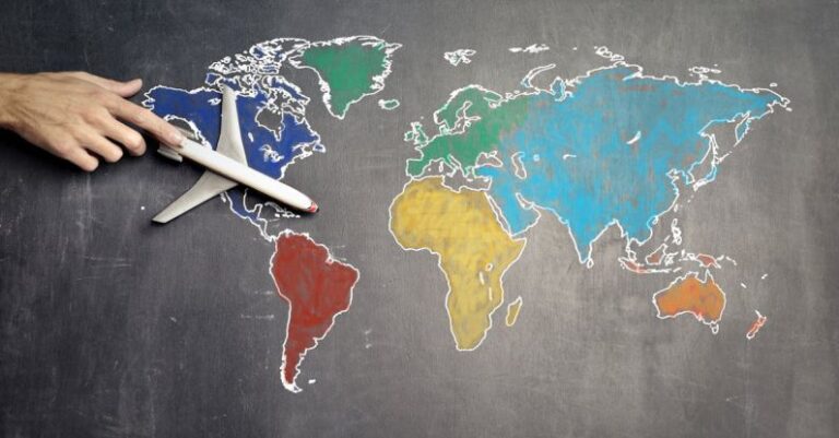 Self-Guided Tours - Top view of crop anonymous person holding toy airplane on colorful world map drawn on chalkboard